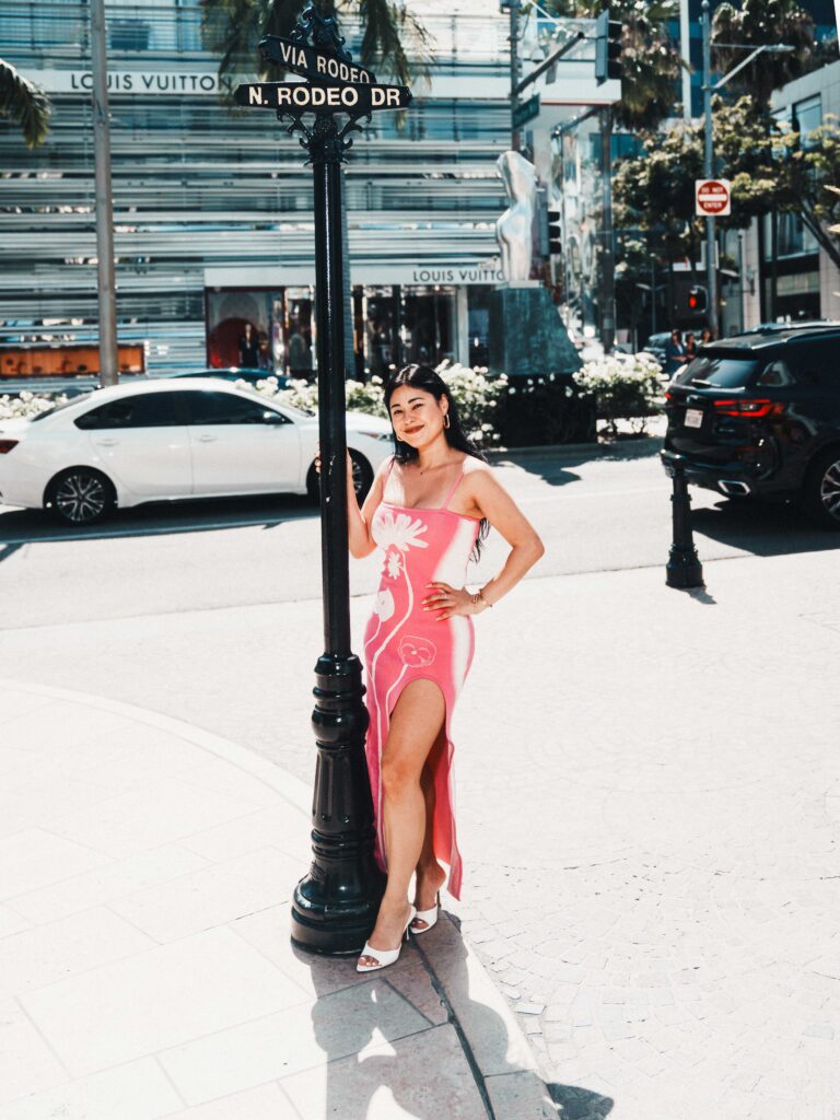 Tammy Veneza posing by Via Rodeo and N Rodeo Drive sign in Beverly Hills, Louis Vuitton storefront background, photographed by Johnny Hann